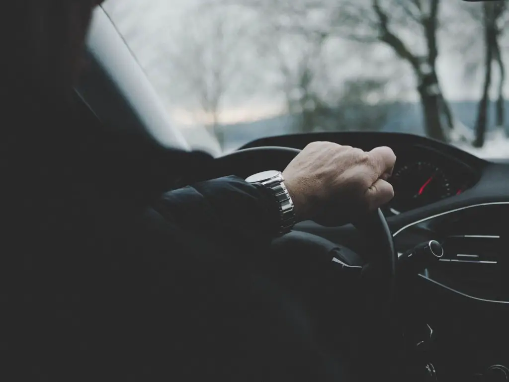 A man's hand grips the steering wheel of a car as he drives. 
